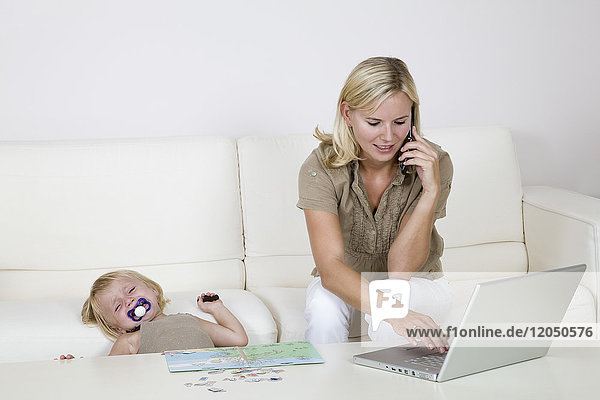 Mutter mit Laptop und Handy  Kleinkind sitzt neben ihr und weint