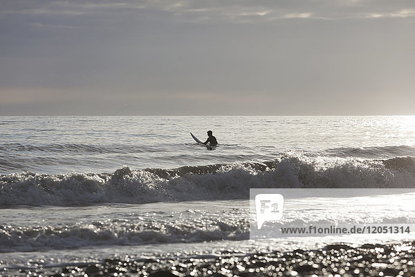 Back Lit Surfer Sitzen auf Surfbrett in Kachemak Bay  Homer  Southcentral Alaska  USA