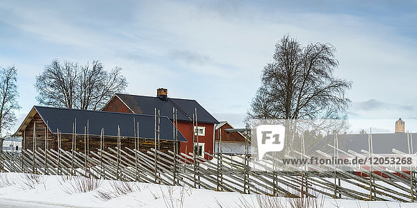 Ein Zaun säumt einen Bauernhof mit roten Gebäuden im Winter; Arjeplog  Provinz Norrbotten  Schweden