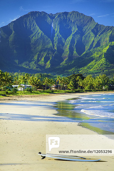 Ein Surfbrett liegt am Strand am Rande des Wassers mit schroffen grünen Bergen und üppigem Laub auf der Insel Kauai; Hanalei  Kauai  Hawaii  Vereinigte Staaten von Amerika