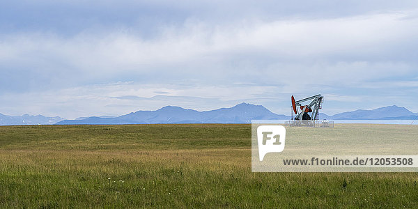 A pump jack at an oil well in a grass field with the Canadian Rocky mountains in the distance; Alberta  Canada