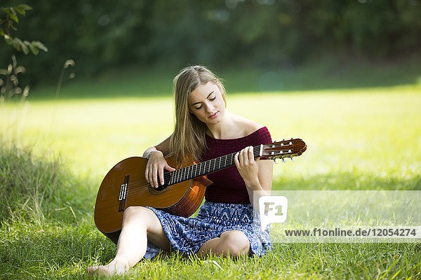 Junge Frau auf der Wiese sitzend  Gitarre spielend