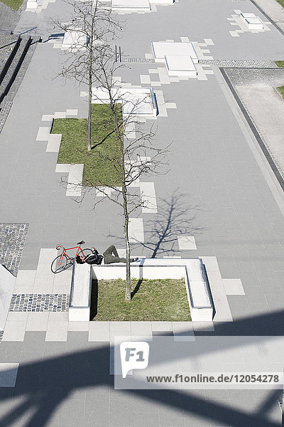 Man relaxing in city skatepark with smartphone next to his bicycle