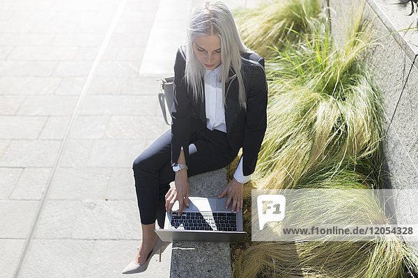 Junge Geschäftsfrau sitzt auf einer Wand in der Stadt mit Laptop