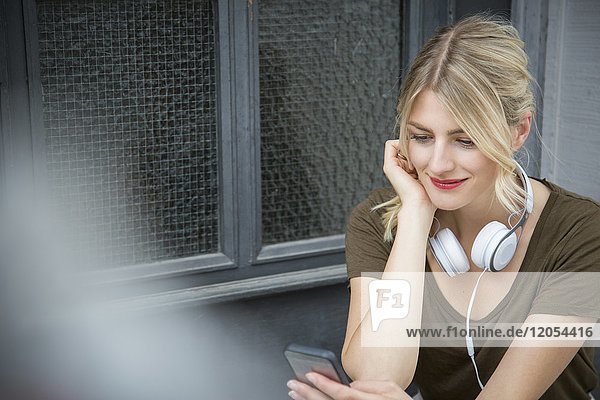 Entspannte junge Frau mit Kopfhörer beim Blick aufs Handy