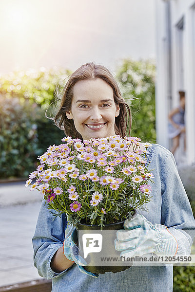 Portrait of smiling woman holding flowerpot in garden