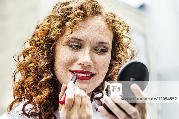 Portrait of freckled young woman applying lipstick