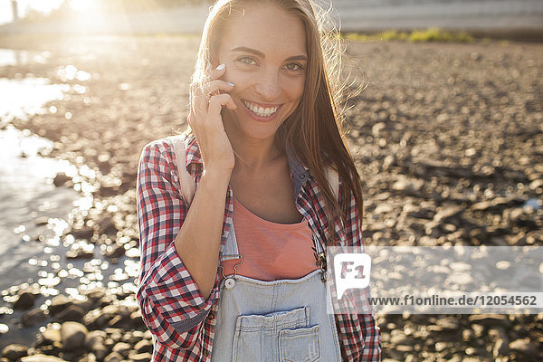 Porträt einer glücklichen jungen Frau auf dem Handy am Flussufer
