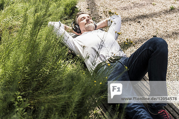 Businessman with headphones lying on a bench