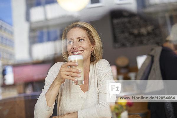 Porträt einer lächelnden Frau  die Latte Macchiato in einem Café trinkt.