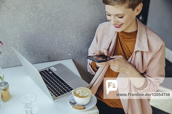 Frau macht ein Smartphone-Foto von ihrem Kaffee in einem Cafe