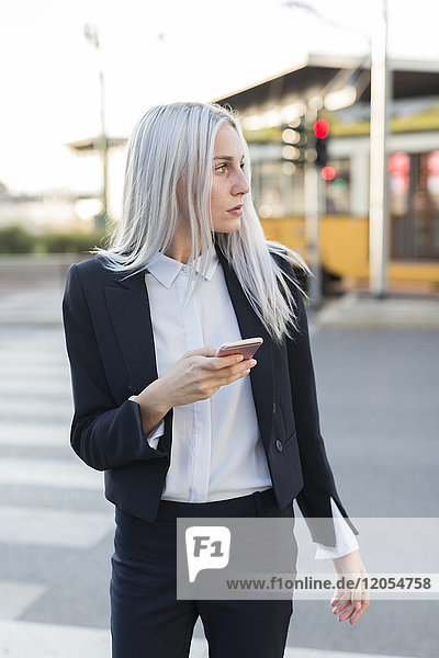Young businesswoman in the city with cell phone looking around