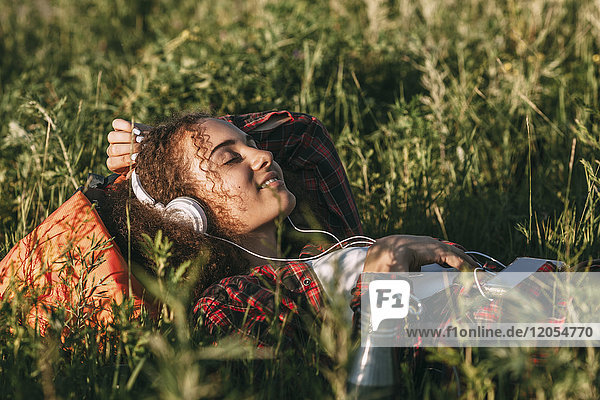 Teenage girl with backpack lying on a meadow listening music with headphones and cell phone