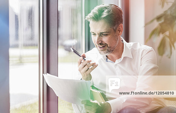 Businessman looking at documents using cell phone