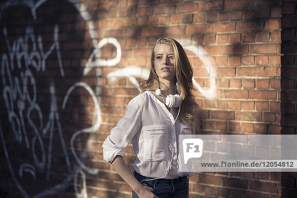 Portrait of young woman with headphones in front of brick wall