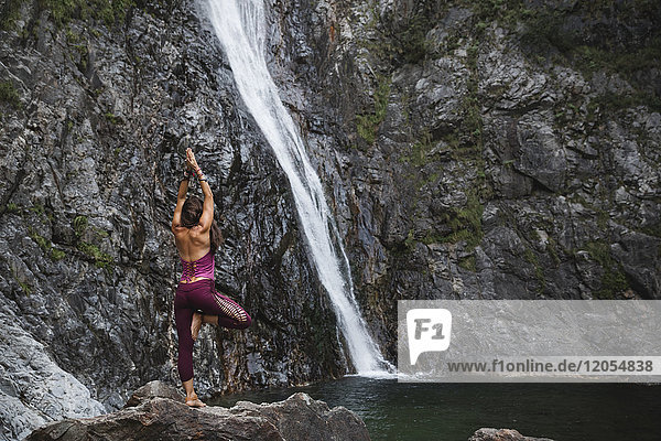 Italien  Lecco  Frau beim Tree Yoga Pose auf einem Felsen in der Nähe eines Wasserfalls