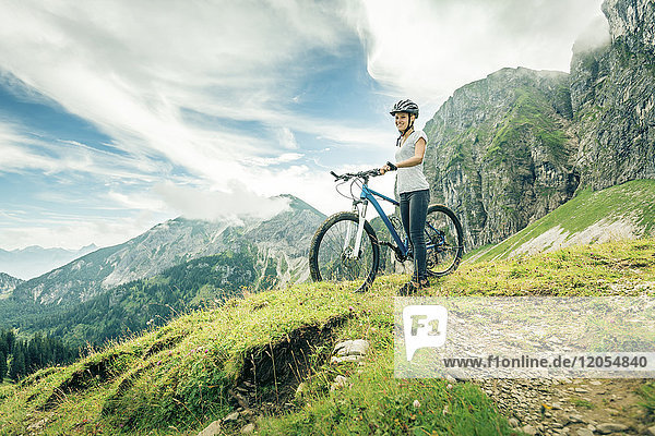 Germany  Bavaria  Pfronten  smiling teenage girl with mountain bike on alpine meadow near Aggenstein