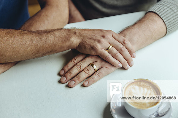 Nahaufnahme der Männerhände mit Eheringen und einer Tasse Kaffee