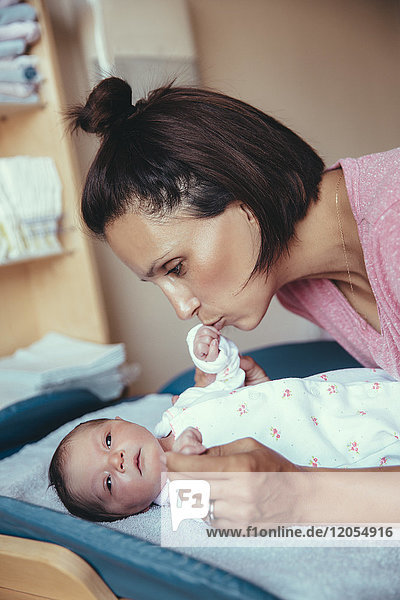 Mutter küsst die Hand ihres neugeborenen Mädchens im Krankenhauszimmer.