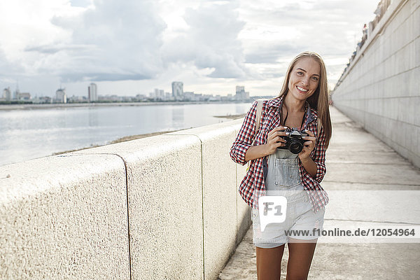 Smiling young woman with a camera at the riverside