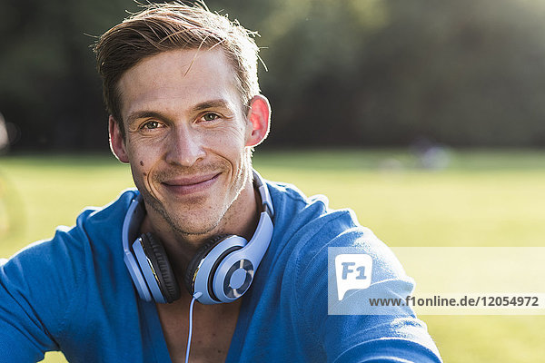 Porträt eines lächelnden Mannes mit Kopfhörer im Park