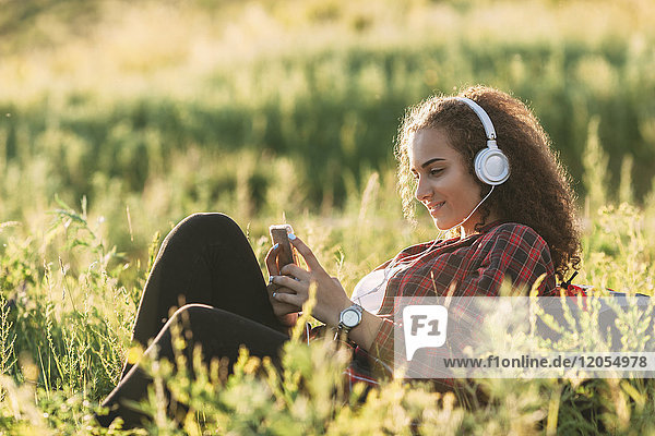Teenage girl listening music with headphones on a meadow looking at cell phone