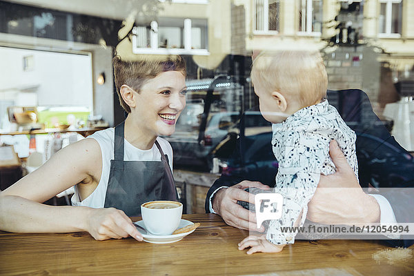 Kellnerin serviert Kaffee für lächelnde Kunden mit Baby im Cafe