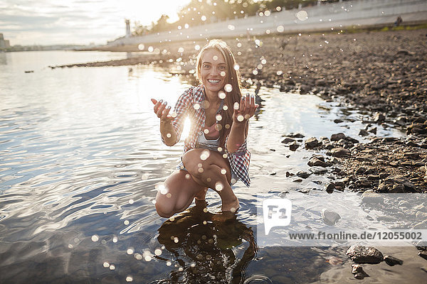 Happy young woman spalshing in a river at sunset