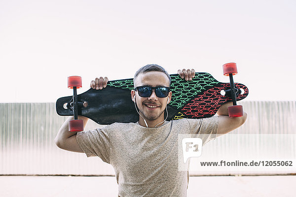 Portrait of confident young man with earbuds carrying longboard