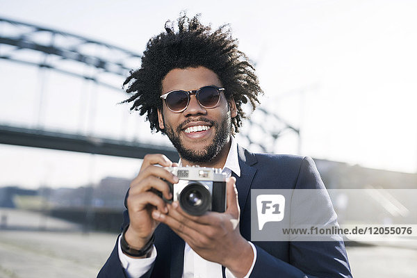 Smiling man in suit at the riverside holding a vintage camera