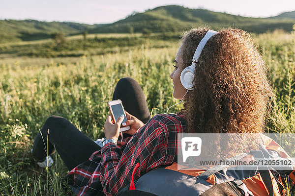 Teenagermädchen mit Rucksack Musik hören mit Kopfhörer auf einer Wiese