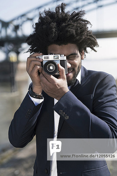 Mann im Anzug am Flussufer beim Fotografieren mit einer Vintage-Kamera