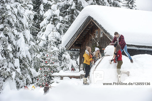 Österreich  Altenmarkt-Zauchensee  Freunde bauen großen Schneemann am Holzhaus auf