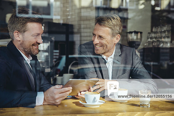 Two smiling businessmen with tablet in a cafe