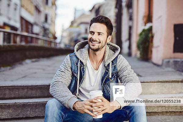 Mann mit Kaffee auf der Treppe sitzend mit Stadt im Hintergrund