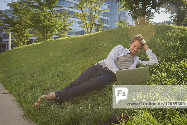 Mann auf Rasen liegend mit seinem Laptop