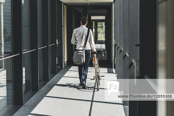 Businessman pushing bicycle in office passageway