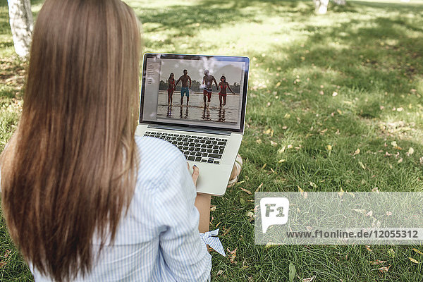 Young woman looking at photography on laptop screen on a meadow