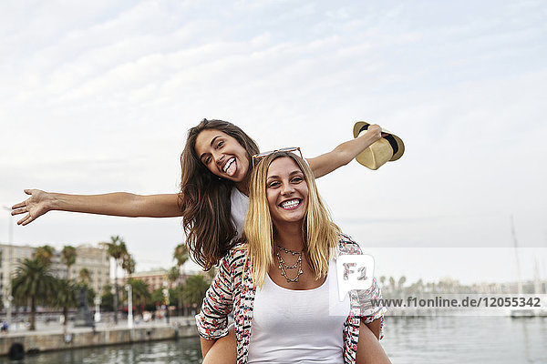 Spain  Barcelona  young woman giving her friend a piggyback ride