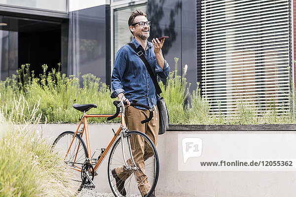 Lächelnder Geschäftsmann mit Handy schiebendem Fahrrad
