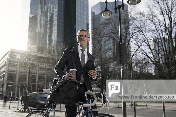Grauhaariger Geschäftsmann mit Fahrrad und Kaffee zum Mitnehmen in der Stadt