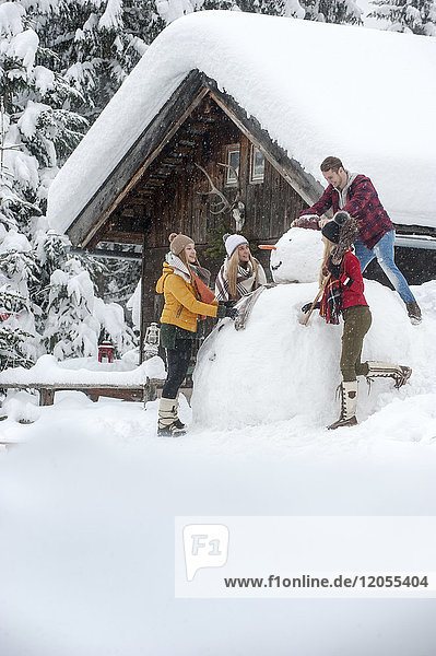 Österreich  Altenmarkt-Zauchensee  Freunde bauen großen Schneemann am Holzhaus auf