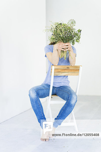 Woman sitting on a chair holding bunch of flowers in front of her face