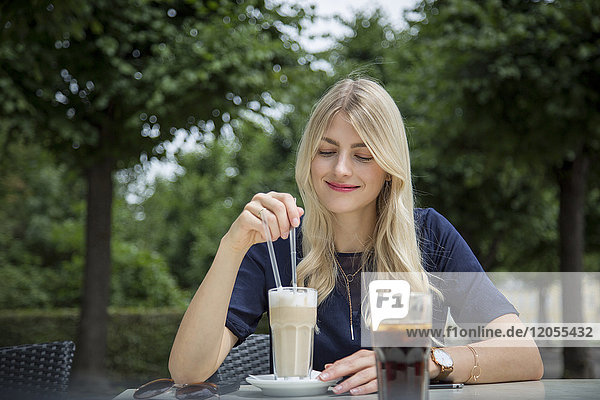 Portrait of blond woman sitting at sidewalk cafe with Latte Macchiato