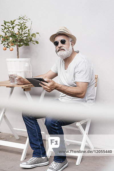 Erwachsener Mann mit Strohhut  der eine Tablette neben dem Tisch mit Orangenbaum hält.