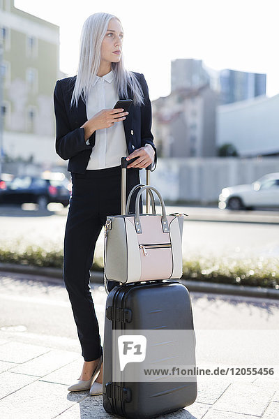 Junge Geschäftsfrau in der Stadt mit Handy und Gepäck