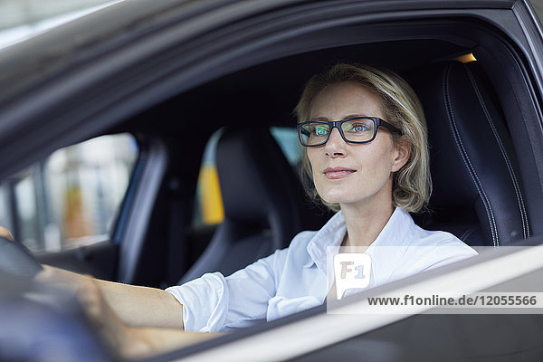 Blonde Geschäftsfrau mit Brille beim Autofahren