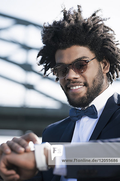 Smiling young man with sunglasses looking at his smartwatch