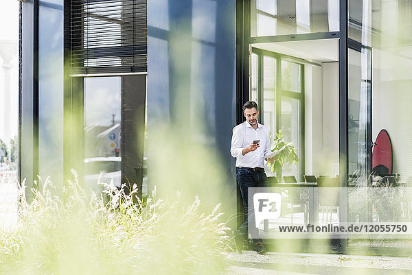 Geschäftsmann vor dem Bürogebäude mit Blick aufs Handy