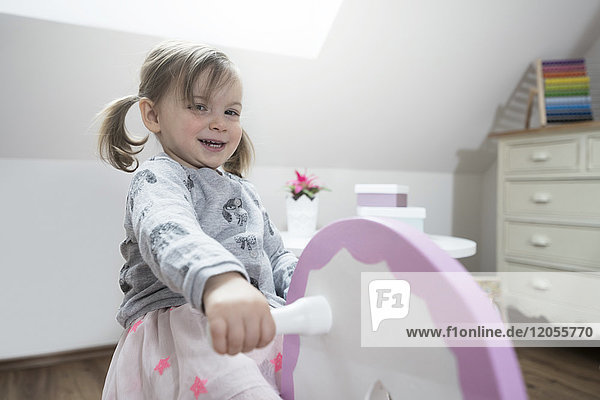 Fröhliches Kleinkind Mädchen schaukelt auf Schaukelpferd im Kinderzimmer